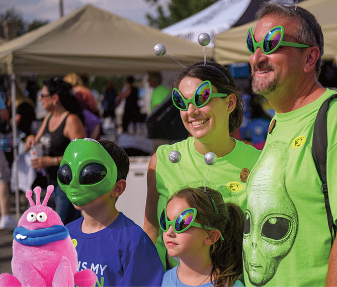 Enlargeable photo of a family wearing green alien masks and glasses with a pink plush alien
