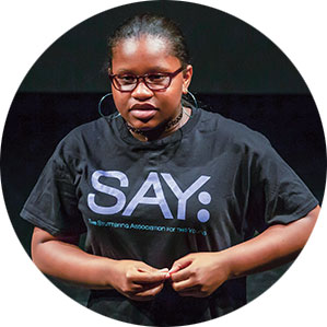 A young woman performing while wearing a t-shirt that says "Say"
