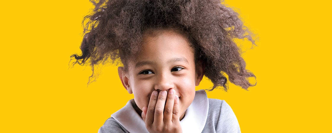 A child smilling as she covers her mouth