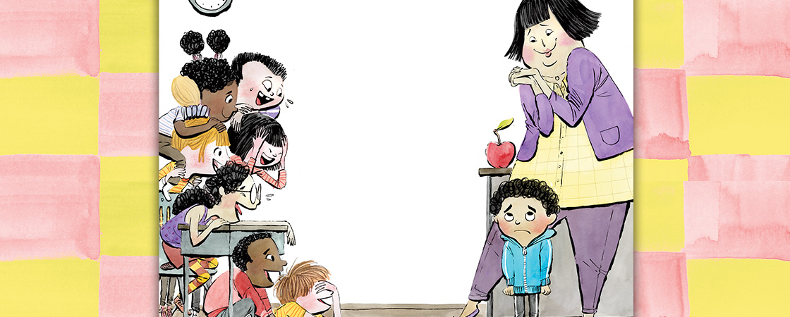 A group of children in a classroom look toward a boy who stands near an adult at a desk